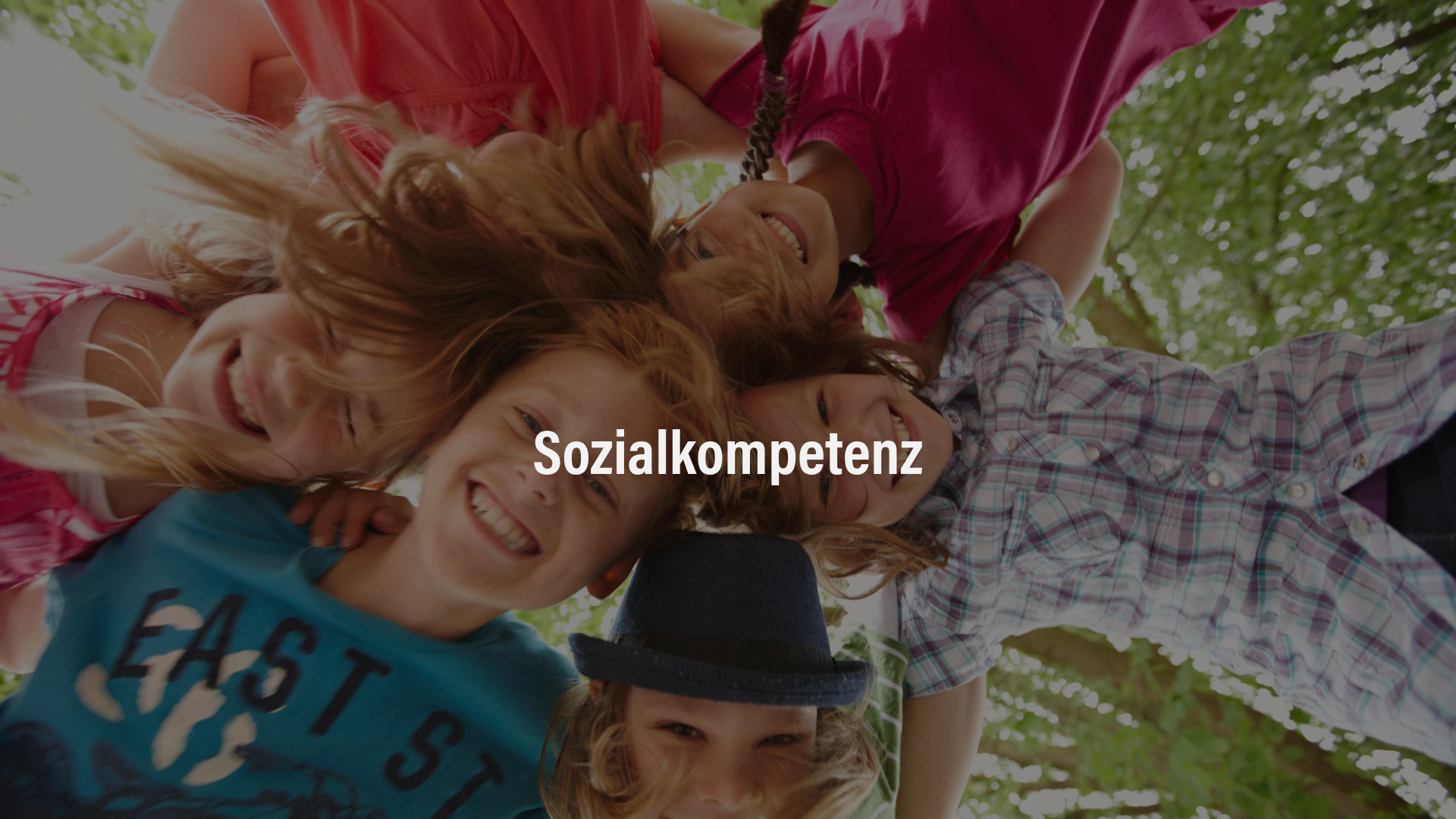 Sozialkompetenz Eine Gruppe von fünf Kindern lacht fröhlich und legt die Köpfe zusammen, aufgenommen aus der Froschperspektive.