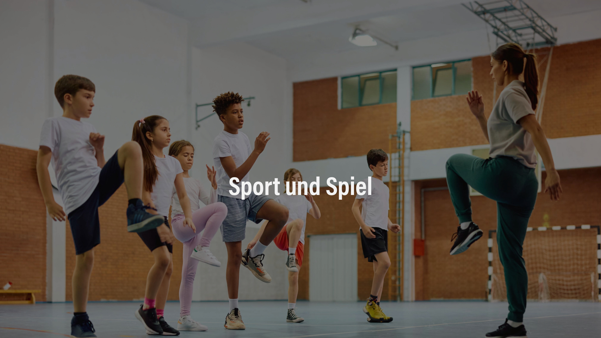 Mehrere Kinder und eine Trainerin üben gemeinsam eine Bewegungseinheit in einer Sporthalle.