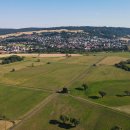 Grüne Felder sind im Vordergrund zu sehen. In der Mitte des Bildes liegen die Häuser der Marktgemeinde Niederaula. Der Himmel ist blau, die Sonne scheint. Am linken Bildrand ist eine ICE-Brücke zu sehen.