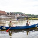 Ein Kanu mit zwei Personen fahren auf der Fulda. Im Hintergrund sind Fachwerkhäuser der Stadt Rotenburg an der Fulda zu sehen.