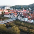 Luftbild über die Stadt Rotenburg an der Fulda mit Blick auf die Fulda, die alte Fuldabrücke und die Fachwerkhäuser der Innenstadt. Im Hintergrund ist ein bewaldeter Berg zu sehen. 