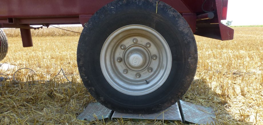 Ein Reifen einer landwirtschaftlichen Maschine steht auf einem Feld. Zwischen Feld und Reifen ist eine Metalleplatte.