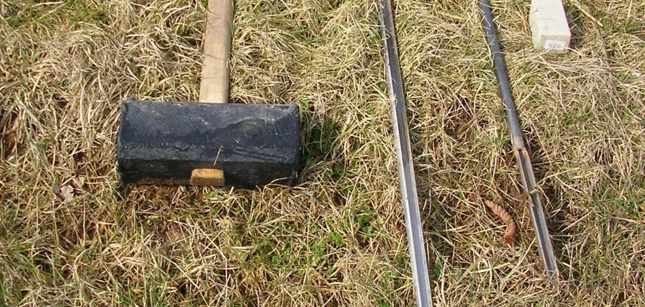 Auf Heu und Gras liegt ein Vorschlaghammer.