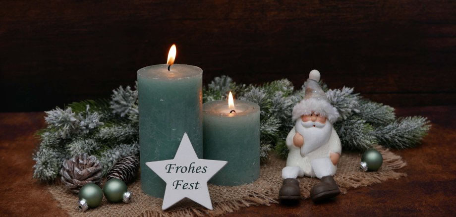 Weihnachtskarte Frohes Fest: Nikolaus vor grünen Kerzen und Tannenzweigen sitzend mit dem Text Frohes Fest auf einem Stern.