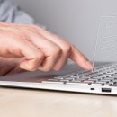 Ein silberner Laptop aus dem Seitenprofil betrachten. Eine Hand klickt mit dem Zeigefinger auf eine Taste. In der Mitte über den Laptoptasten ist ein Formular-Symbol zu sehen.