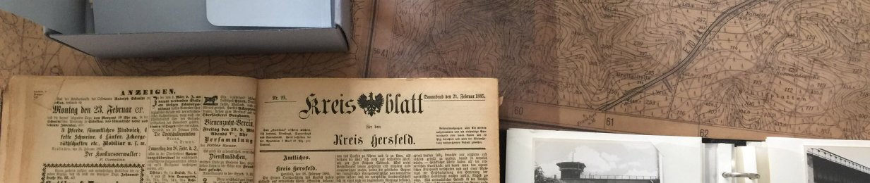 Links oben ein Karton, der halb geöffnet ist und worin alte Zeitungen liegen. Im Hintergrund liegt eine antike Karte, unten links eine historische Ausgabe des Kreisblatts von 1885. Rechts unten ein Fotoalbum mit schwarz-weiß Fotos vom Bahnhof Bebra und einem Tunnel. Oben in der Mitte liegt ein Dia, daneben steht Dorflinden.