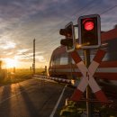 Bahnübergang im Sonnenuntergang. Schranken sind unten, ein roter Zug fährt durch.