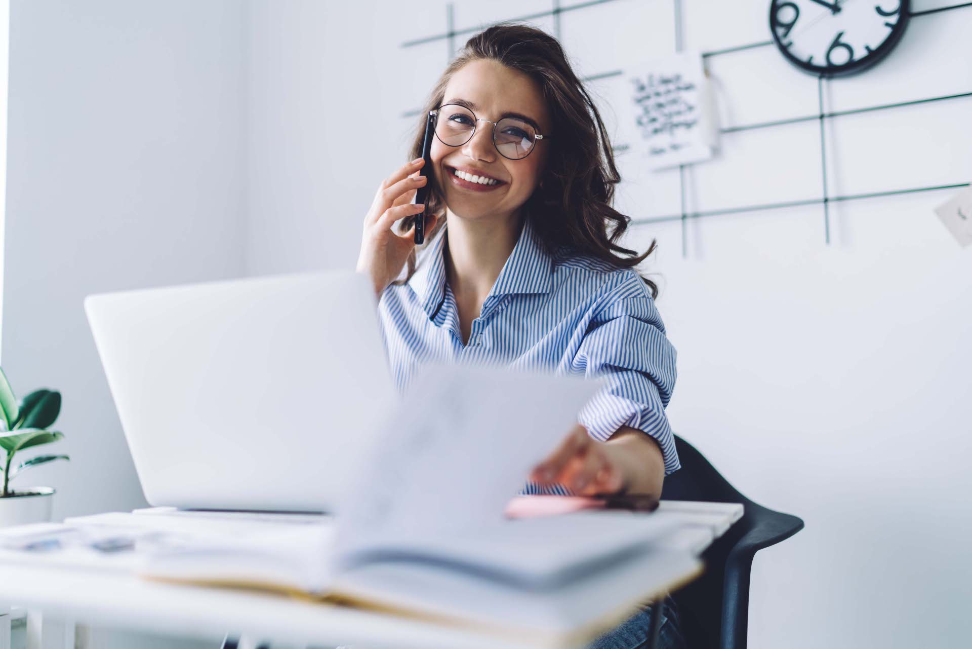 Junge Frau mit Brille telefoniert lächelnd am Schreibtisch, vor ihr ein Laptop und Unterlagen – symbolisch für den Arbeitsalltag in der Kreisverwaltung.