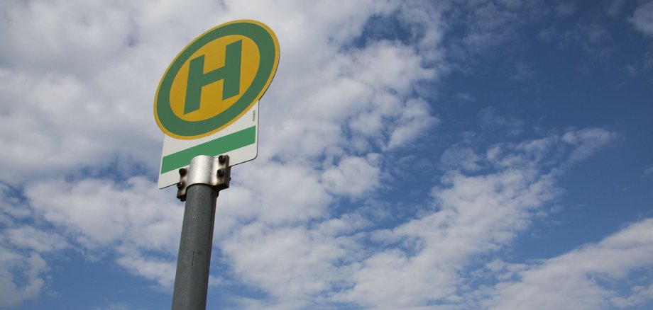 Ein Bushaltestellenschild steht vor einem blauen Himmel mit ein paar Wolken.