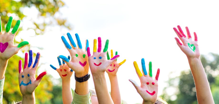 Viele hochgehaltene Arme mit Händen. Auf den Händen sind bunte Smileys gemalt, die Finger sind farbig gemalt.