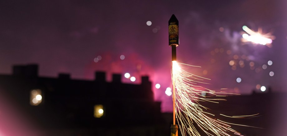 Man sieht wie eine bunte Silvesterrakete gerade gezündet wird. Es ist Nacht.