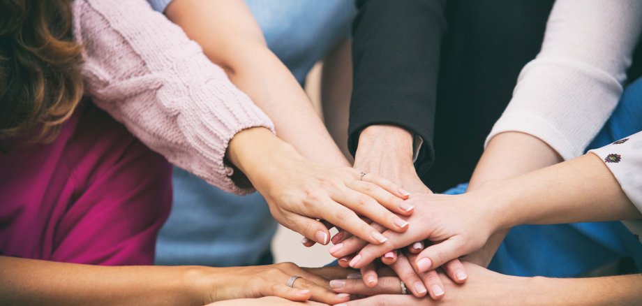 Eine Gruppe von Frauen steht im Kreis, die Hände sind in der Mitte und liegen aufeinander.