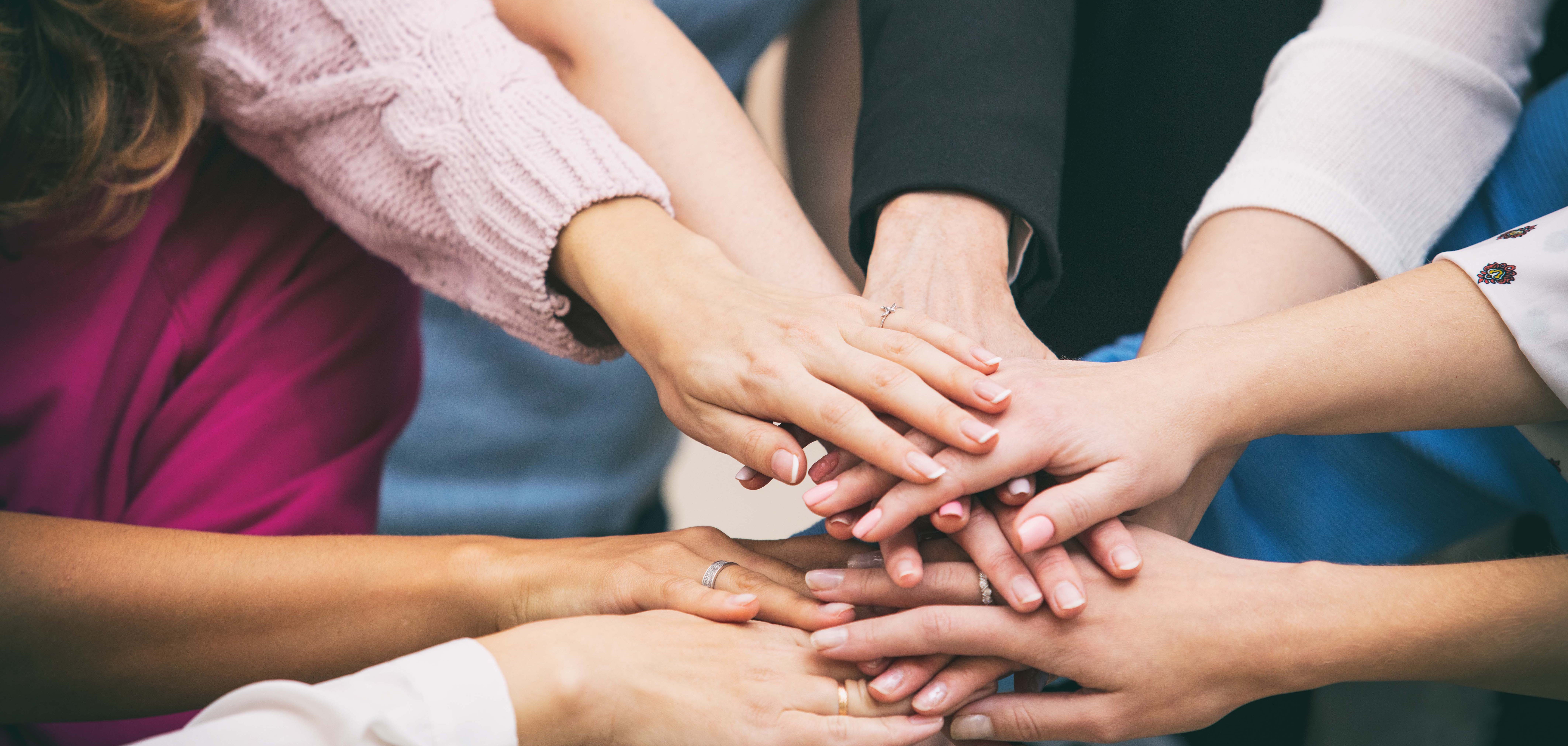 Eine Gruppe von Frauen steht im Kreis, die Hände sind in der Mitte und liegen aufeinander.