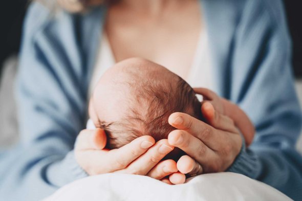 Eine Frau hält ein neugeborenes Baby liebevoll mit beiden Händen am Hinterkopf.