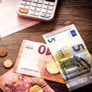 Euro Banknoten und Münzen liegen auf einem Tisch. Zudem liegt dort auch noch ein Taschenrechner.