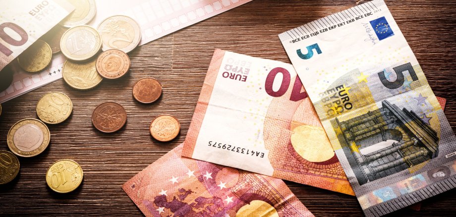 Euro Banknoten und Münzen liegen auf einem Tisch. Zudem liegt dort auch noch ein Taschenrechner.