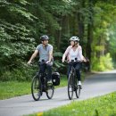 Zwei Radfahrer, ein Mann und eine Frau, fahren auf dem Fulda-Radweg R1 durch den grünen Wald.