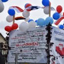 Ein Motivwagen mit vielen Luftballons in rot, blau und weiß. An den Wagen sind ebenfalls deutsche, finnische und polnische kleine Flaggen angebracht. Ein Banner mit der Aufschrift "willkommen" in vielen verschiedenen Sprachen hängt am Wagen.