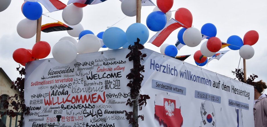 Ein Motivwagen mit vielen Luftballons in rot, blau und weiß. An den Wagen sind ebenfalls deutsche, finnische und polnische kleine Flaggen angebracht. Ein Banner mit der Aufschrift "willkommen" in vielen verschiedenen Sprachen hängt am Wagen.