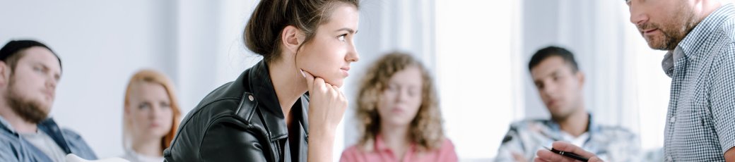 Rebellierende Teenagerin hört einem Sozialpädagogen zu während einer Gruppentherapiestunde mit anderen Jugendlichen, die Probleme haben.
