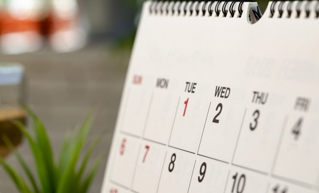 Nahaufnahme eines Teils einer Kalenderseite. Tischkalender steht auf einem Holzschreibtisch.