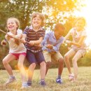 Vier Kinder, Mädchen und Jungen, ziehen gemeinsam an einem Tau. Sie spielen in der Natur.