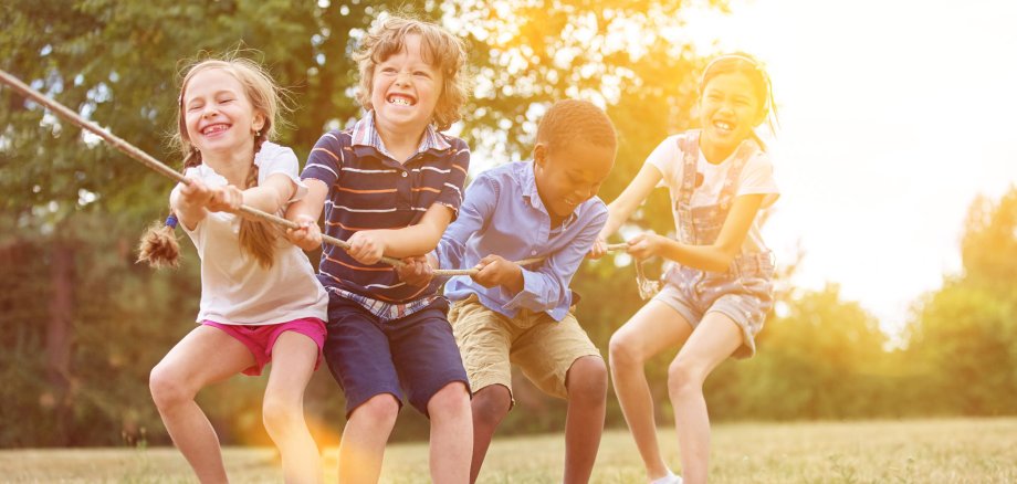 Vier Kinder, Mädchen und Jungen, ziehen gemeinsam an einem Tau. Sie spielen in der Natur.