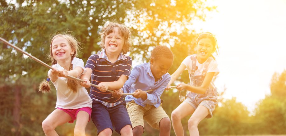 Vier Kinder, Mädchen und Jungen, ziehen gemeinsam an einem Tau. Sie spielen in der Natur.