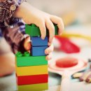 Eine Kinderand spielt mit Bauklötzen. Im Hintergrund sind weitere Spielsachen zu sehen.