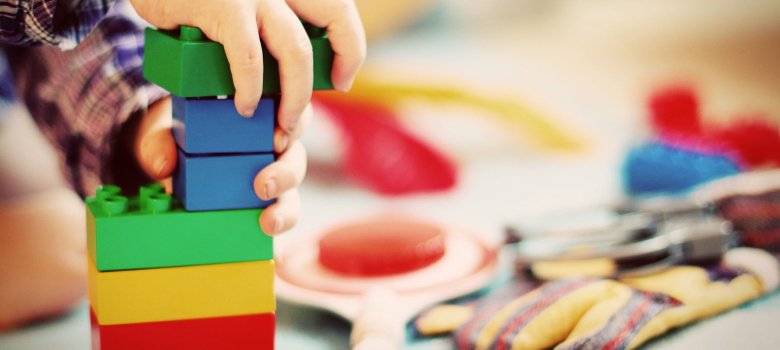 Eine Kinderand spielt mit Bauklötzen. Im Hintergrund sind weitere Spielsachen zu sehen.