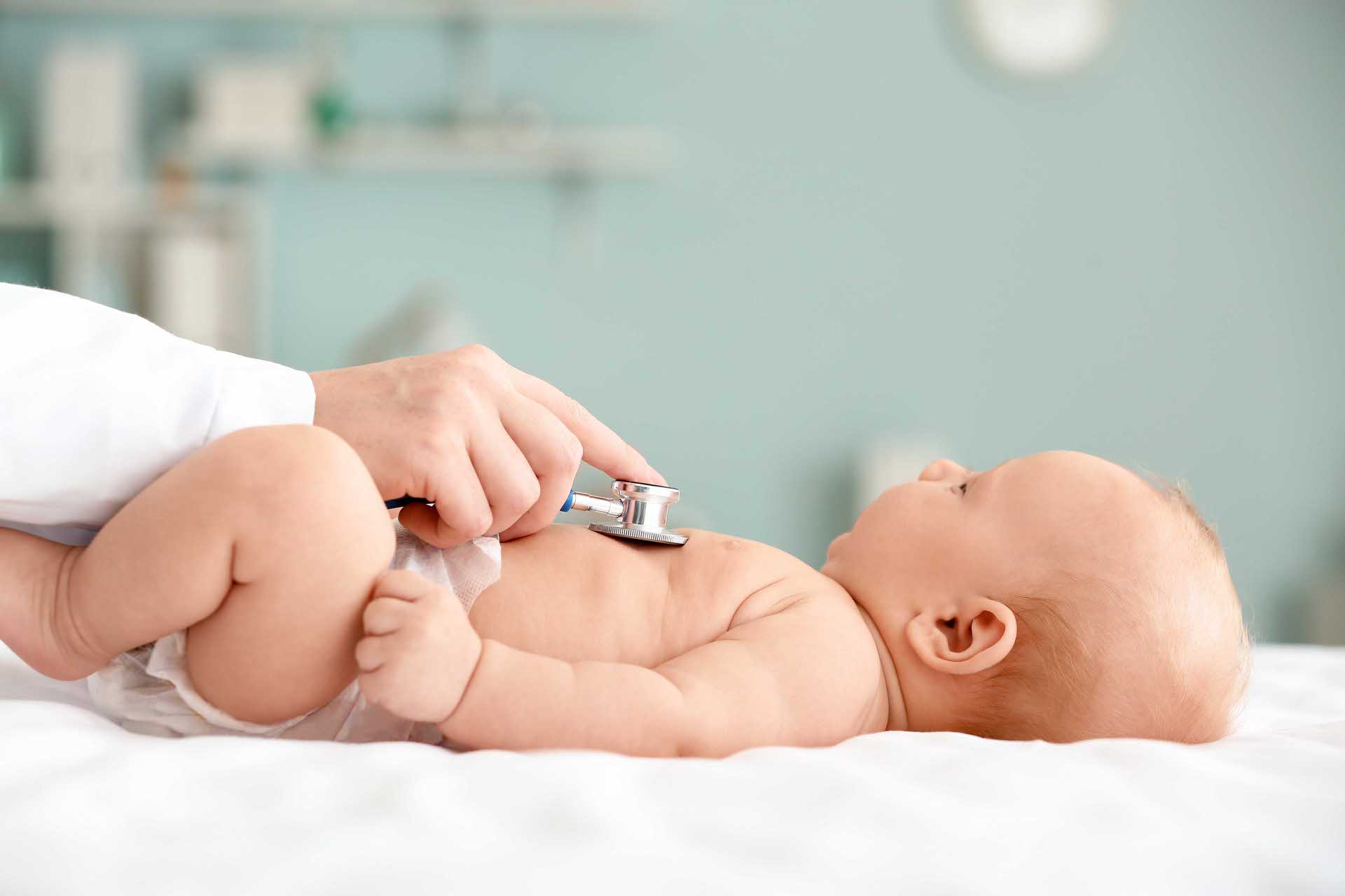 Ein Baby liegt auf dem Rücken, während ein Arzt oder eine Ärztin mit einem Stethoskop die Brust abhört.