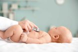 Ein Baby liegt auf dem Rücken, während ein Arzt oder eine Ärztin mit einem Stethoskop die Brust abhört.