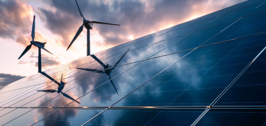 Im Vordergrund sieht man eine Solaranlage. Im Hintergrund sieht man zwei Windräder.