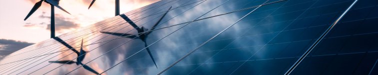 Im Vordergrund sieht man eine Solaranlage. Im Hintergrund sieht man zwei Windräder.
