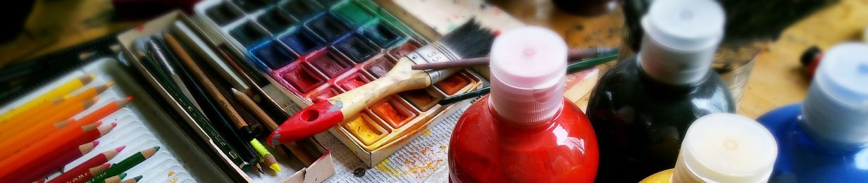 Auf einem Tisch liegen Buntstifte in vielen verschiedenen Farben und ein bunter Tuschkasten. Weitere Utensilien zum Malen, wie ein Pinsel und Farben stehen ebenfalls auf dem Tisch.