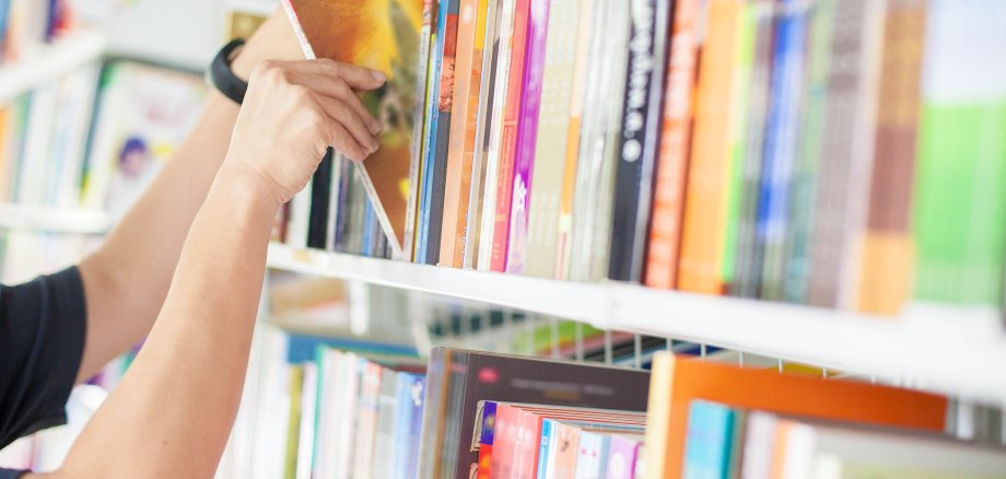 Eine männliche Hand greift eines von vielen Büchern, die in einem Bücherregal in einer Bücherei stehen.