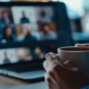 Virtual meeting concept with a close-up of hands holding a coffee mug in front of a laptop screen showing a video conference