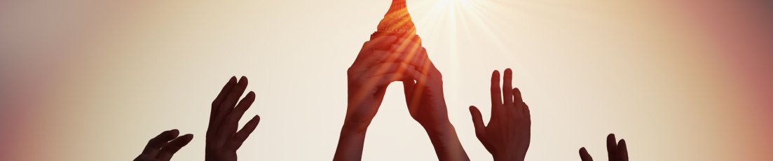 Viele Hände halten gemeinsam einen Pokal in die Höhe. Im Hintergrund geht die Sonne unter.