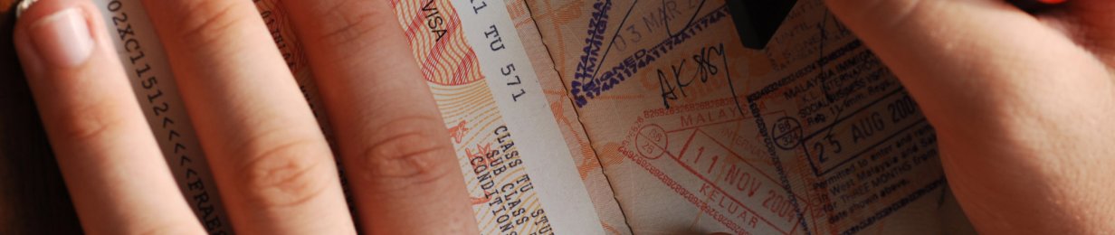 Nahaufnahme eines Reisepasses mit einer Hand darauf und einer weiteren, die einen Stempel hinzufügt. Erkennbar sind viele Stempel und ein Australien-Visa.