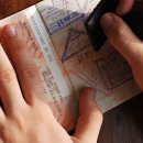 Nahaufnahme eines Reisepasses mit einer Hand darauf und einer weiteren, die einen Stempel hinzufügt. Erkennbar sind viele Stempel und ein Australien-Visa.