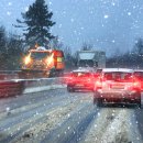 Einige Fahrzeuge fahren auf einer schneebedeckten Autobahn. Es schneit. Auf der linken Fahrspur ist zudem ein Streu- und Räumfahrzeug zu sehen.