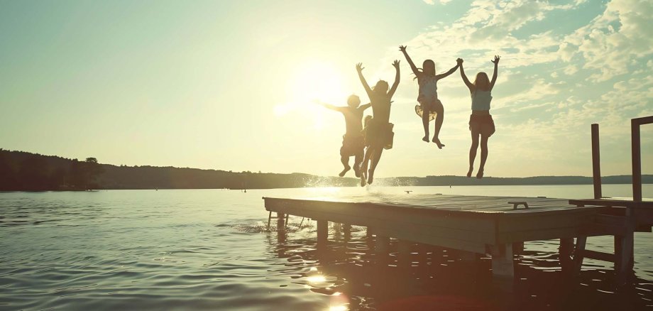 Group of teenage kids jumping off the dock into the lake togethe