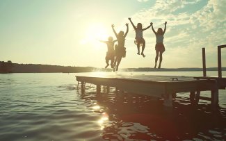 Group of teenage kids jumping off the dock into the lake togethe
