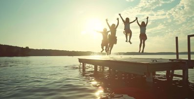 Group of teenage kids jumping off the dock into the lake togethe