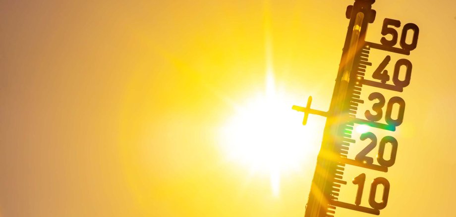 Ein Thermometer zeigt Temperaturen über 30 Grad Celsius an, im Hintergrund scheint grell die Sonne durch einen orange-gelben Himmel.