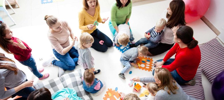 Mehrere Eltern und Kleinkinder sitzen auf dem Boden und spielen mit bunten Spielmaterialien.