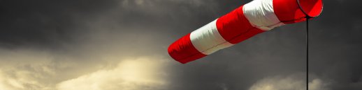 Rot-weiß wehender Windsack. Im Hintergrund dunkle Wolken. 