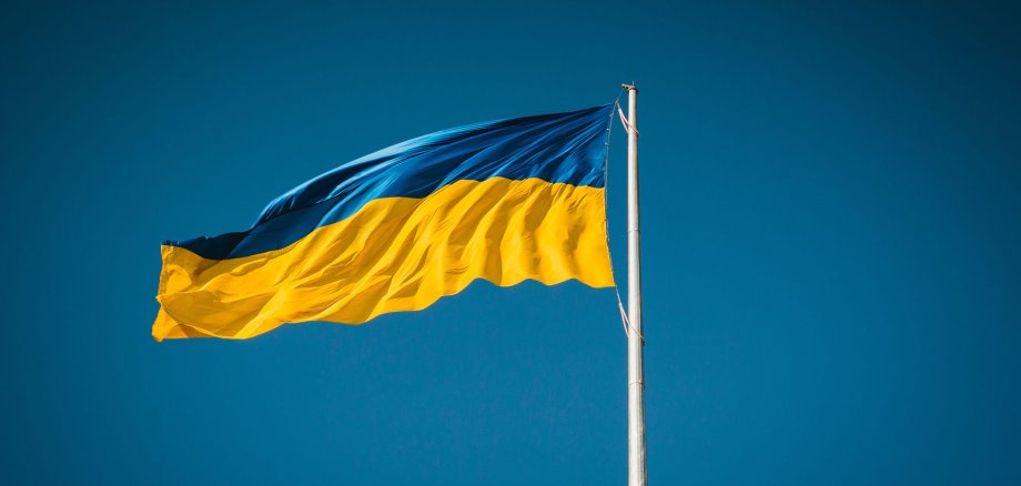 Eine Ukraine-Flagge weht im Wind. Im Hintergrund ist blauer Himmel.