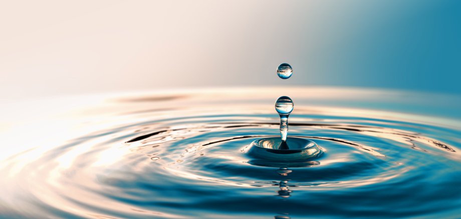 Nahaufnahme eines Wassertropfen, der ins Wasser tropft, hochspritzt und Wellen erzeugt.