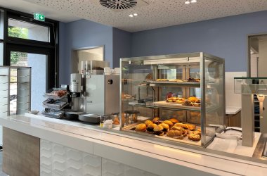 In der Kantine des Landratsamtes liegen belegte Brötchen aus. Man sieht eine Kaffeemaschine und kleine Snacks.